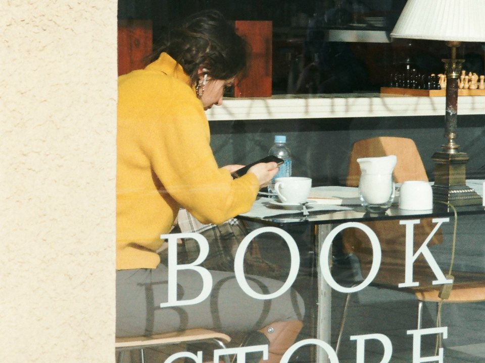 A woman reading at a table, seen through the window of a bookstore café.