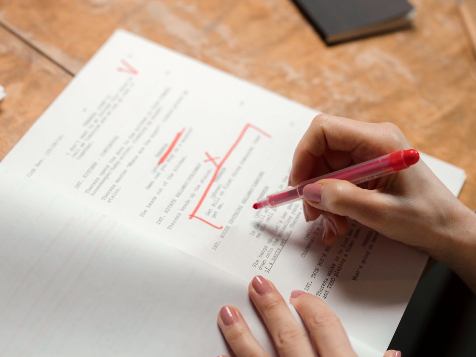 A hand marking up a printed typescript with a red pen, corrections in the margin.