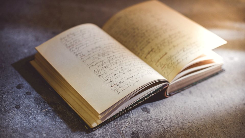 An old notebook lying open on stone, both pages covered in close handwriting.