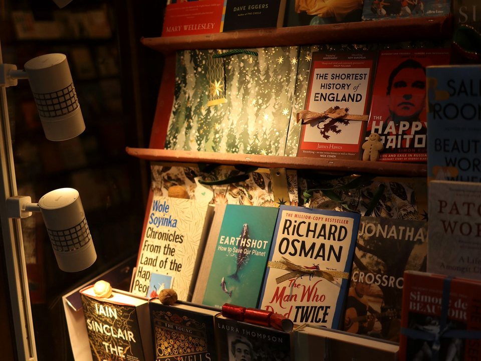 A lit bookshop window display, new hardbacks and paperbacks standing face out on wooden shelves.