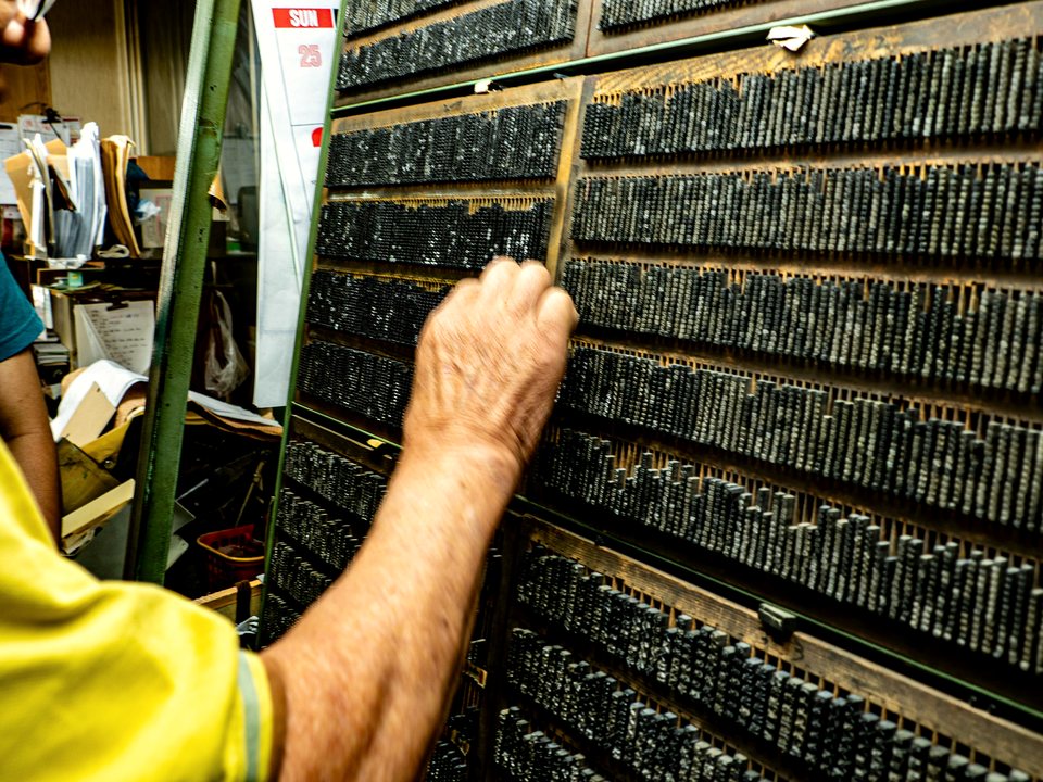 A printer at a wall of letterpress type cases, reaching into a drawer of lead sorts.